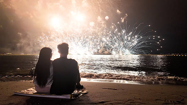 istock Romantic couple sits in a warm embrace, mesmerized by the dazzling fireworks display exploding over the sea, celebrating Christmas or New Year 2249483531