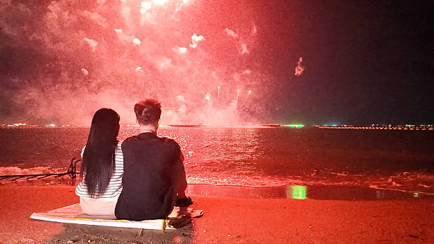 istock Romantic couple sits in a warm embrace, mesmerized by the dazzling fireworks display exploding over the sea, celebrating Christmas or New Year 2249483553