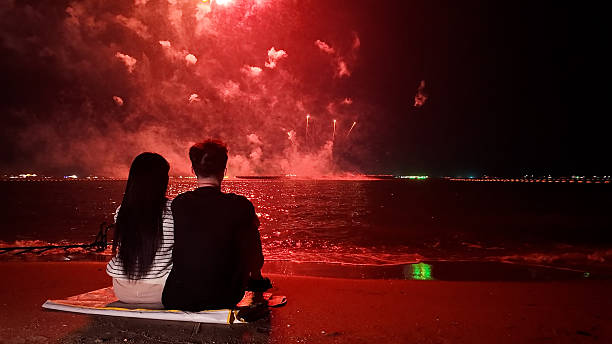 istock Romantic couple sits in a warm embrace, mesmerized by the dazzling fireworks display exploding over the sea, celebrating Christmas or New Year 2249483566