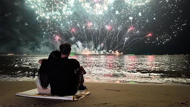 istock Romantic couple sits in a warm embrace, mesmerized by the dazzling fireworks display exploding over the sea, celebrating Christmas or New Year 2249483688