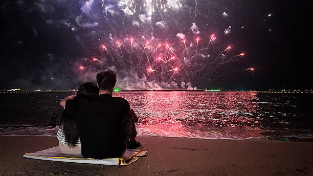 istock Romantic couple sits in a warm embrace, mesmerized by the dazzling fireworks display exploding over the sea, celebrating Christmas or New Year 2249483716
