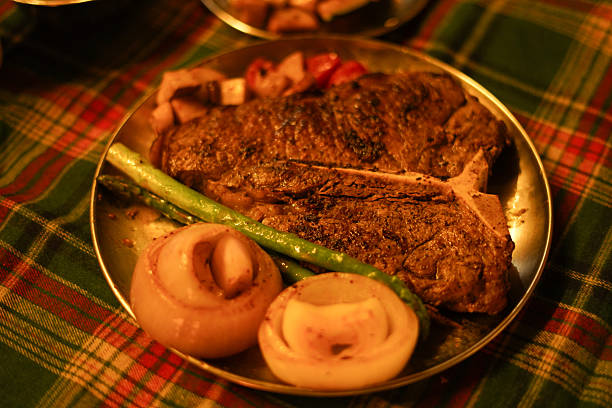 Grilled beef medallions with herbs and cherry tomatoes on a wooden table, cutlery next to it. Close-up.