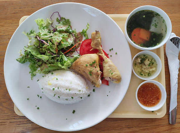 A neatly arranged lunch set featuring steamed rice, boiled chicken, fresh salad, dipping sauce, and a warm soup.