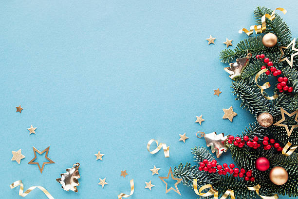 istock Festive Christmas background or greeting card with green pine branches, red berries and shiny golden decorations on blue top view, flat lay. 2249488083