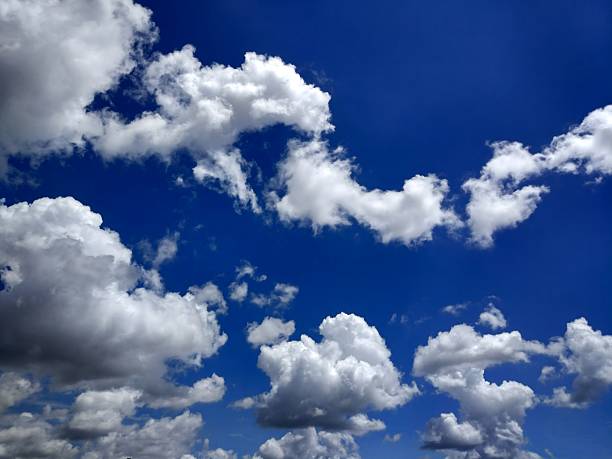 The photographer captures fluffy white cumulus clouds forming dynamic patterns against a deep blue sky to create a vivid and serene atmospheric scene.