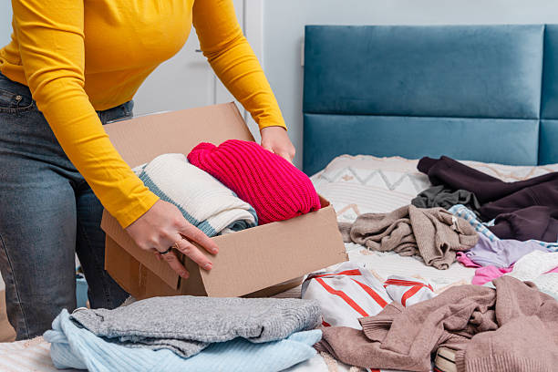 istock A young woman sorting clothes and packing into cardboard boxes. Donations for charity, help low income families, declutter home, sell online, moving moving into new home or recycling 2249493941