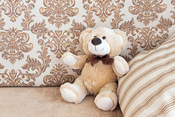 istock Brown teddy bear sitting on beige cozy sofa with pillows in the background. 2249494502