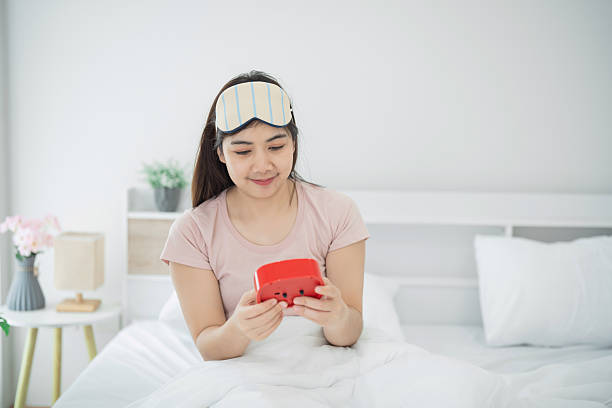 Young woman in sleep mask playing handheld game console in bed, relaxed morning routine in cozy bedroom with soft light and peaceful atmosphere