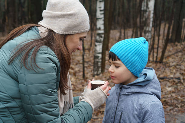 Caring mother sharing a warm drink with her son on a cold day in the forest