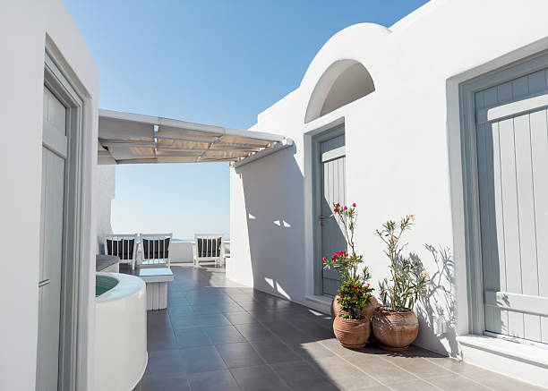 Opened beige double door leading to a terrace with tiled floor and old pottery. Old house balcony overlooking Aegean sea and Cyclades islands.