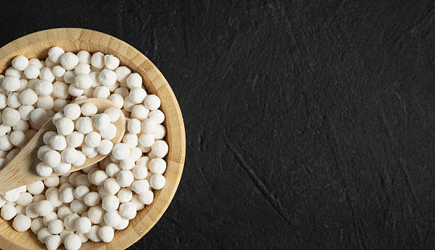 istock Organic tapioca pearls in wooden bamboo bowl on black table top view with copy space. Spoon scooping white dry tapioca pearls, cooking ingredient, gluten free food, healthy eating. 2249503394