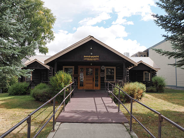 Jackson, WY - Sep 22, 2025: Frontal view of a dark historic log cabin (American Legion Post 43) with a wooden ramp and surrounding trees.