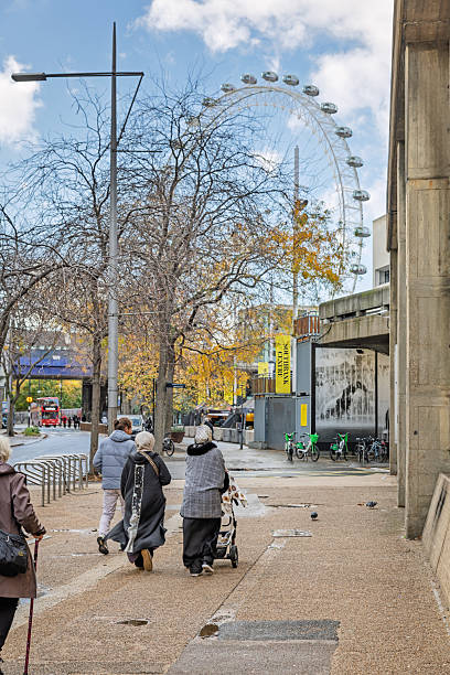 Belvedere Road, London, England, United Kingdom, Europe - November 2nd 2025: Locals and tourists strolling in the autumn sun along the south side of the River Thames with a view of the London Eye.
