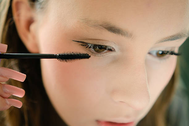 A beautiful teenage girl applying mascara to her eyelashes in a close-up shot. Self-applied makeup highlighting youthful style and confident grooming.