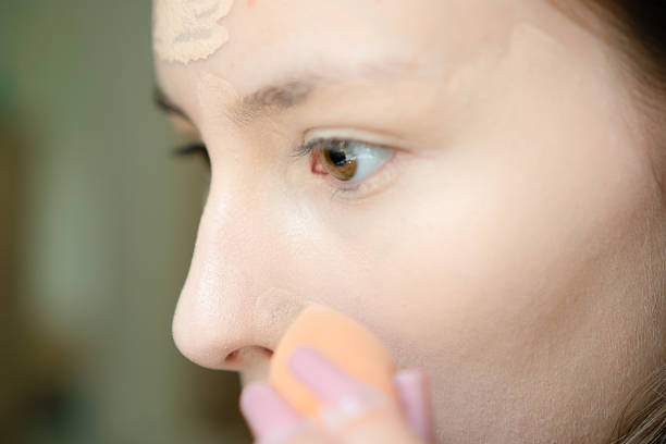 Close-up of a stylish teenage girl applying foundation on her face independently. Young girl focused on skin care and beauty routine, looking polished and trendy.