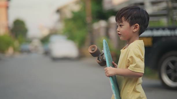 four-year-old Asian child learns to skateboard with guidance from his older sister during the early evening after school. The moment captures family bonding, childhood development, active outdoor play, and supportive sibling relationships. Perfect for themes related to parenting, education, sports learning, childhood lifestyle, evening activities, and family connection.