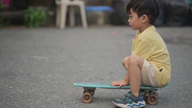 four-year-old Asian child learns to skateboard with guidance from his older sister during the early evening after school. The moment captures family bonding, childhood development, active outdoor play, and supportive sibling relationships. Perfect for themes related to parenting, education, sports learning, childhood lifestyle, evening activities, and family connection.