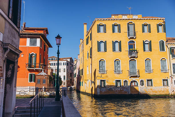 Traditional architecture with vibrant yellow and orange facades reflecting in the calm canal water on a sunny day in Italy