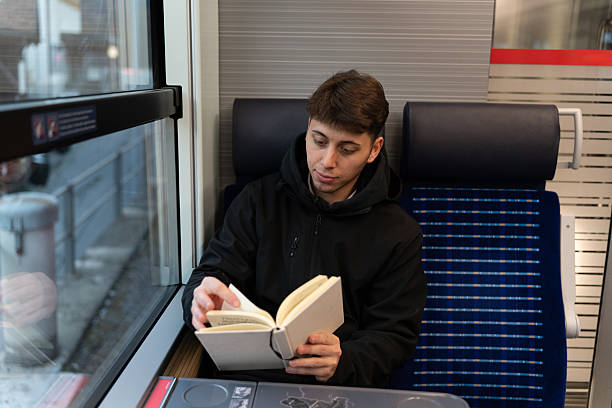 istock Young man reading book traveling on public transport train 2249513471