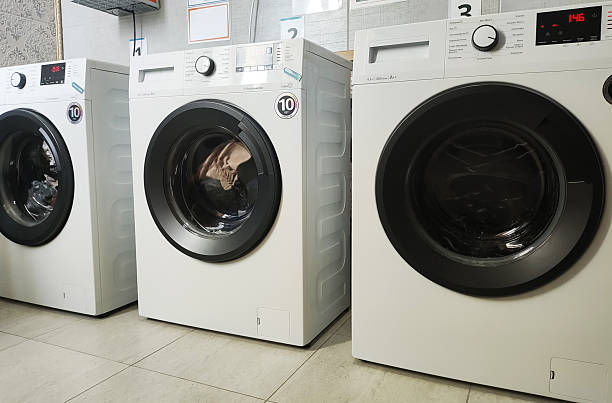 istock Row of three modern white washing machines with black doors and control panels in laundry room interior. Appliances on tiled floor, ready for use or display. 2249514785