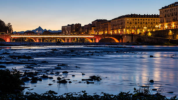 The autumn season transforms the lush, leafy foliage of trees not only into different colors, but also into simpler shapes, where the branches and trunk of the tree, its main frameworks, emerge. Preparing for the bare structure of winter. Here's Turin's main public park of Valentino, along the river Po, at dusk. In the background  the bridge Vittorio Emanuele I and the Monviso peak. Also the waters flow seems to reflect this transformation into the winter simplicity.