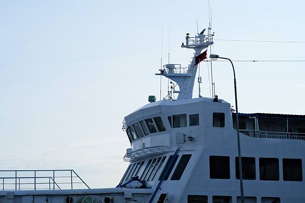 istock Close-up of a ferry's bridge and upper deck with navigation equipment and antennas, docked under clear skies at a harbor. 2249521008