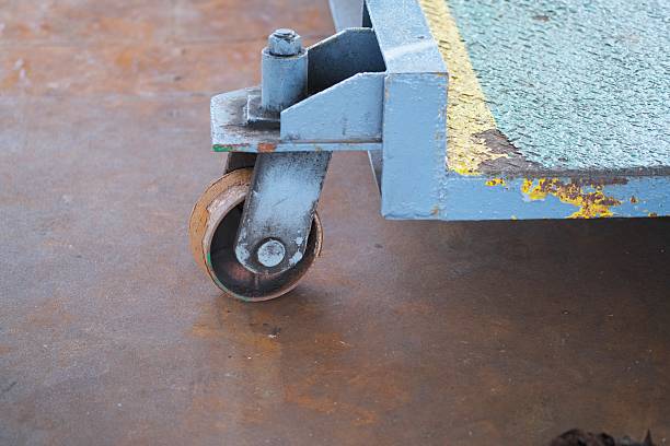Close-up of a worn caster wheel attached to a blue industrial cart with chipped paint, positioned on a rust-colored metal floor.