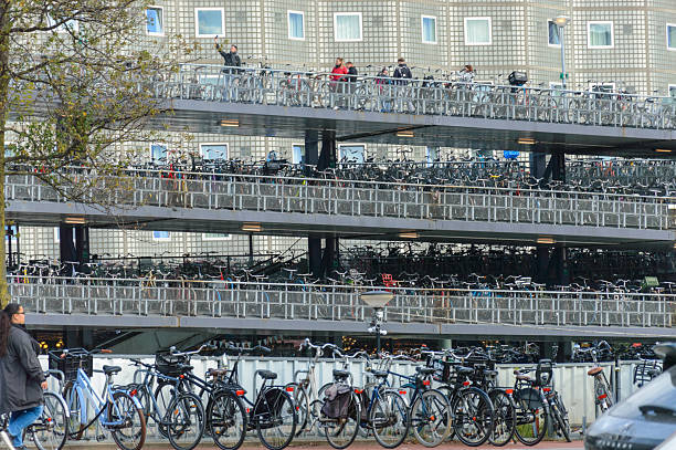 This photograph showcases a multi-story bicycle parking garage in Amsterdam, Netherlands, filled with rows upon rows of bicycles. The image captures the city's commitment to cycling as a sustainable mode of transportation and features people on an upper level using the facilities. The building's facade provides a background for this vibrant urban scene.