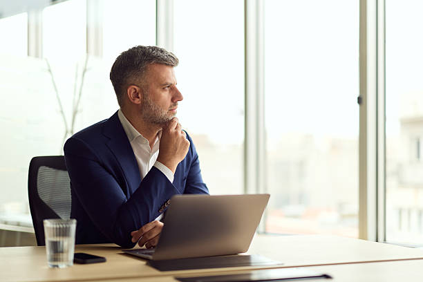 istock Thoughtful Business Professional At Modern Office Desk With Laptop By Window 2249531200