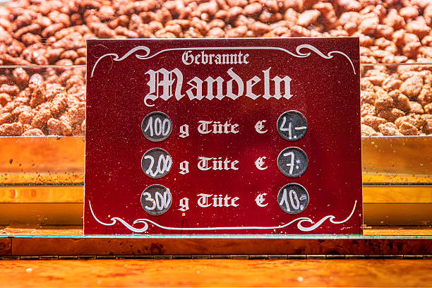 A red sign displaying prices for different portion sizes for roasted almonds in front of a tray with gebrannte mandeln at a christmas market stall