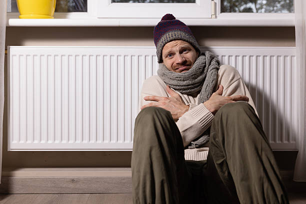 istock freezing man with hat and scarf in front of radiator in cold room at home. heating problems 2249539103