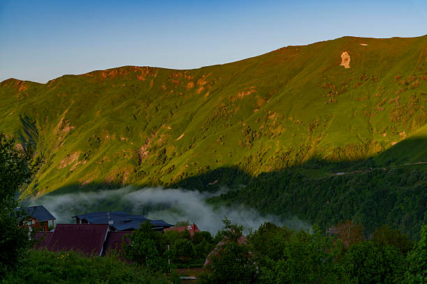 Low fog drifts through a deep green valley while village rooftops catch the first sunlight.