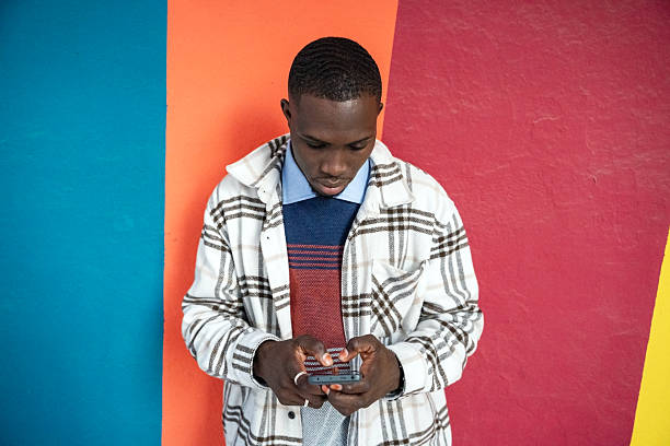 istock Young man engaged in texting with mobile phone against vibrant colored wall in an urban setting 2249541301