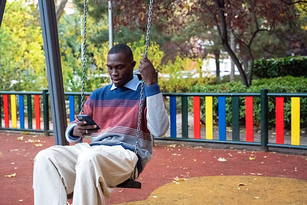 Young man enjoys a quiet moment on a swing while using his smartphone in a vibrant park