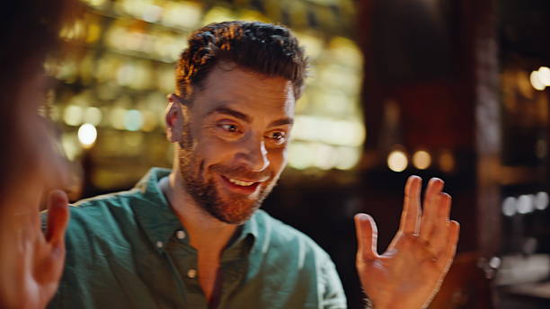 Joyful colleagues gathering in bar enjoying relaxed friendly communication closeup. Group friends talking joking laughing in dark restaurant. Smiling happy people meeting at weekend evening in pub.