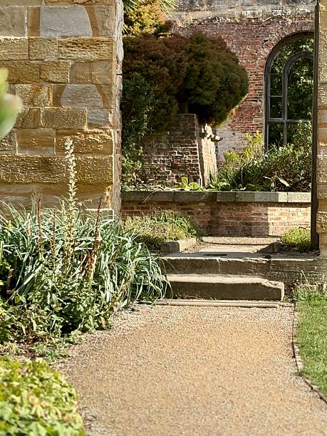 istock A sunlit garden path leads toward stone steps framed by old walls and lush greenery. Warm tones, soft shadows, and an arched ruin in the background create a peaceful, historic atmosphere. 2249542975