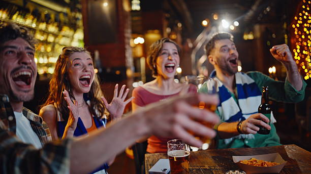 istock Excited students cheering sport game in modern pub drinking beer closeup. 2249545386