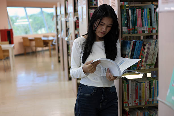 istock Asian female student reading a book from a library shelf, education lifestyle, studying, knowledge development and exploring information in a quiet and modern learning environment. 2249546563