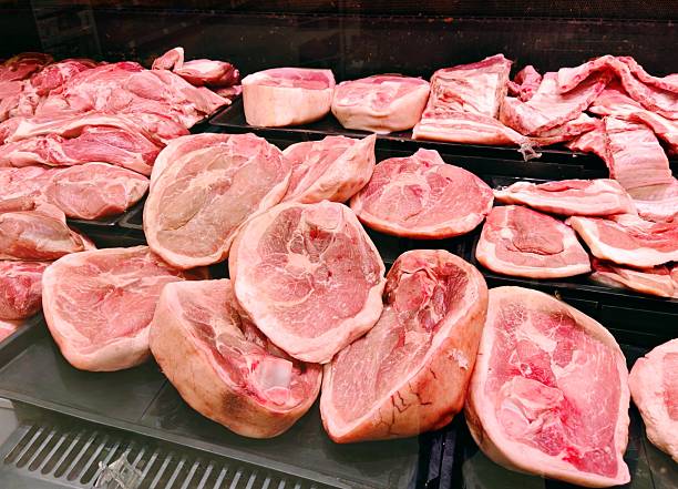 Fresh Raw Pork Cuts in Butcher Shop Display. Assorted chilled pork cuts including chops, ribs and shoulder neatly arranged on black trays in butcher shop counter. Meat and food concept.