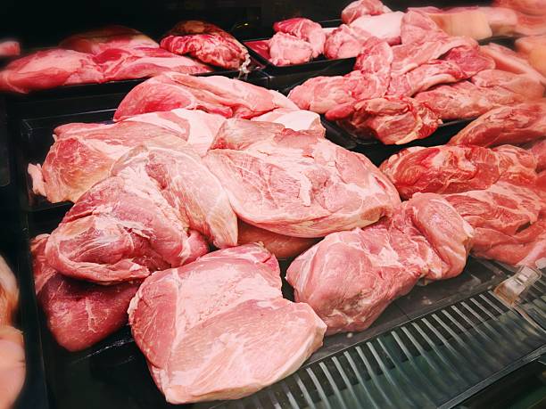 Fresh Raw Pork Cuts in Butcher Shop Display. Assorted chilled pork cuts including chops, ribs and shoulder neatly arranged on black trays in butcher shop counter. Meat and food concept.