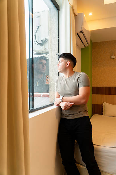 istock Man looking trough the window in his bedroom 2249548010