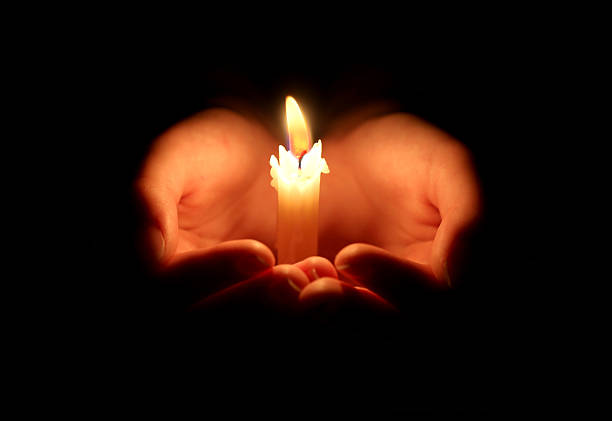 istock burning candle and hands protect the flame so that it does not go out. Black background. 2249548972