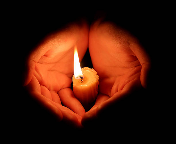 istock burning candle and hands protect the flame so that it does not go out. Black background. 2249548985