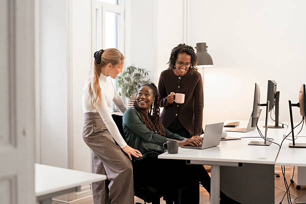 istock Three colleagues in a bright office share a friendly moment around a laptop, coffee mugs nearby, representing teamwork and collaboration 2249550488