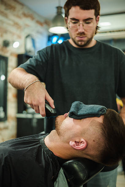 istock Barber shaving client's beard with electric razor 2249551792