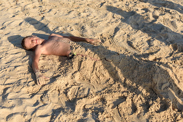 A boy with glasses lies on a towel on the beach to sunbathe in the sand
