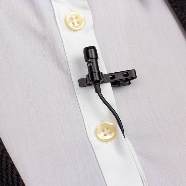 istock A compact black lav mic is secured on a white buttoned shirt, capturing the setup for professional audio recording. 2249559480