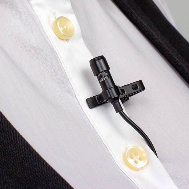 istock A compact black lav mic is secured on a white buttoned shirt, capturing the setup for professional audio recording. 2249560189