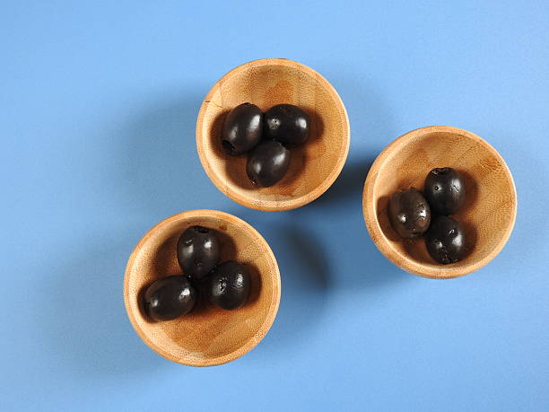 istock Set of black olives in wooden elements on a blue background 2249568953