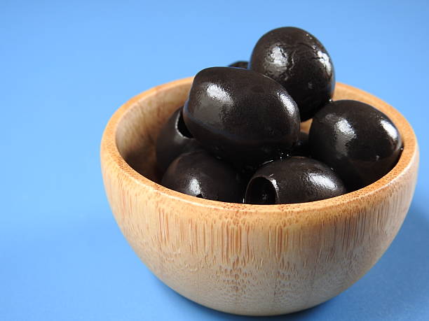 istock Set of black olives in wooden elements on a blue background 2249568977